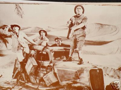Movie still picture of the stooges and a driver with a 1940s taxi stuck in the desert sand