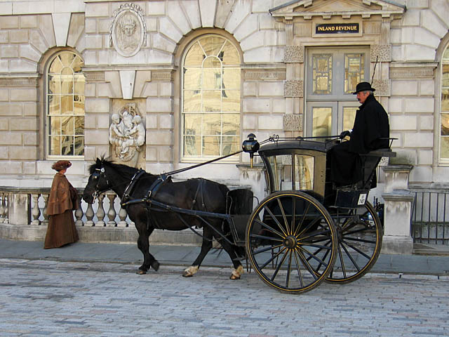 A horse drawn hansom cab with the driver riding high up in the rear of the carriage